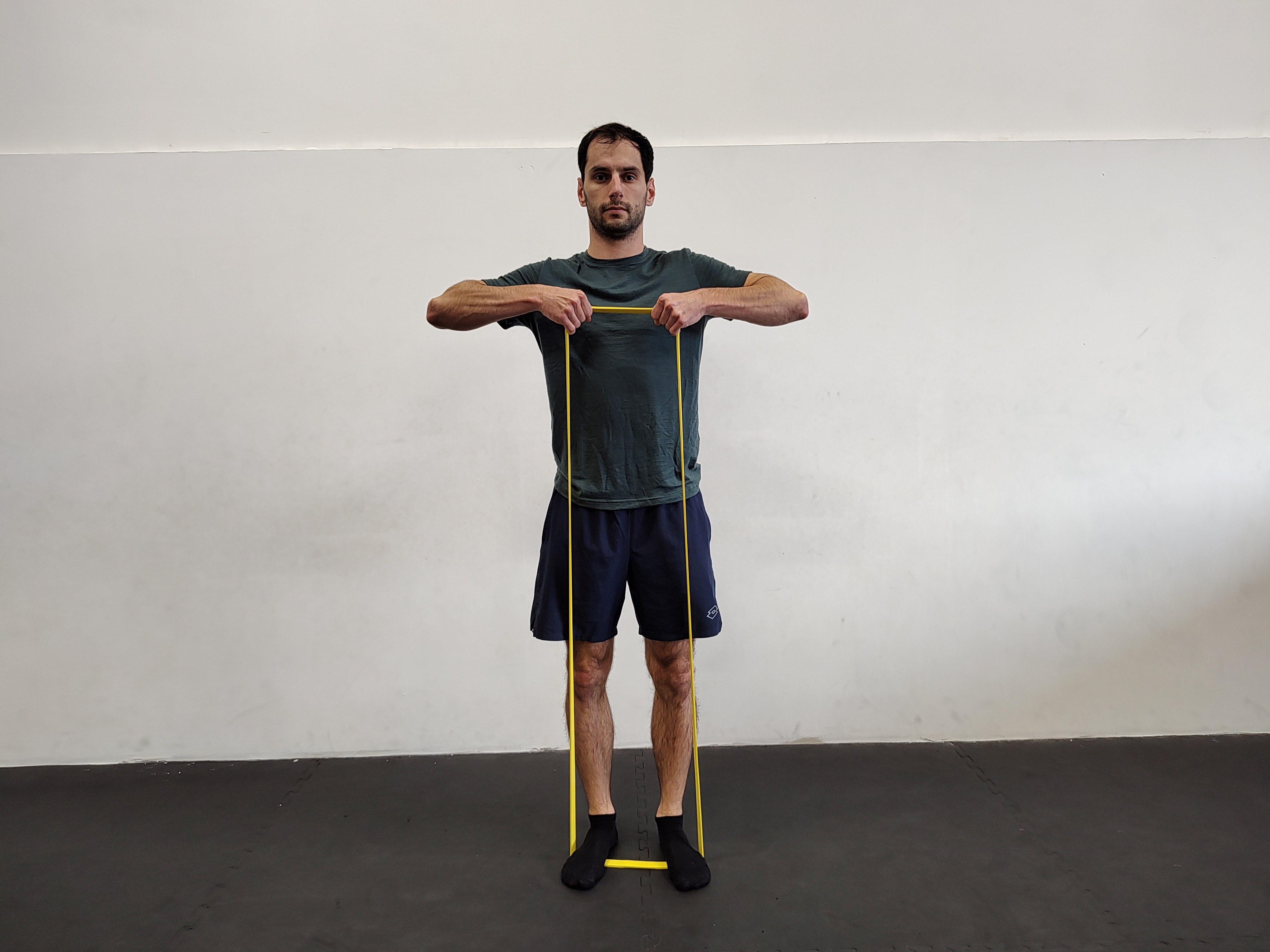 Muž v tělocvičně cvičí přítahy ve stoje s expandérem.